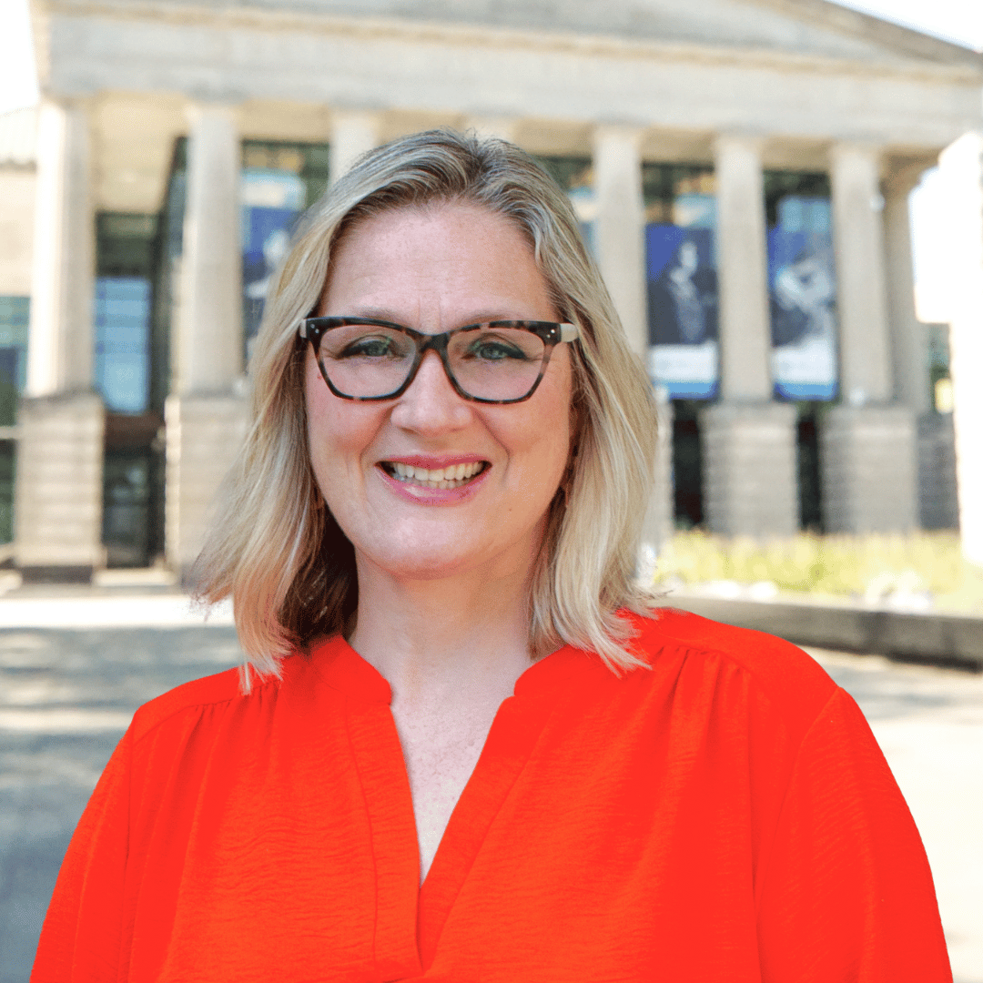 Headshot of Michelle Bradley outside the Martin Marietta Center for the Performing Arts wearing a coral blouse and dark framed glasses.