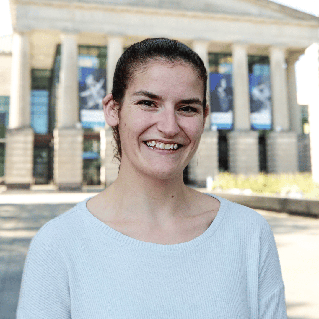 Headshot of Kara Shoup in front of the Martin Marietta Center for the Performing Arts wearing a light blue top with her hair pulled back. 