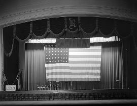 Black and white photo from the 1930's of the interior of Raleigh Memorial Auditorium with a large American flag hanging over the stage.