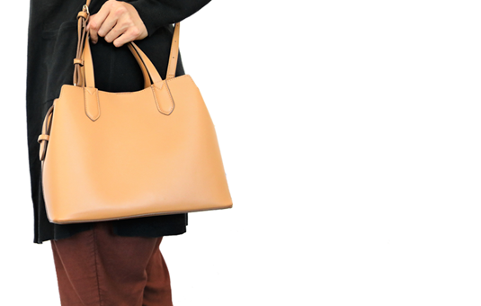 A person is shown holding a medium size brown purse up against their waist