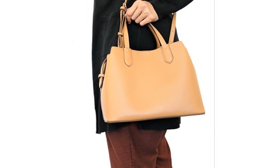 A person is shown holding a medium size brown purse up against their waist