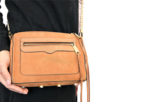 A photo of a small brown crossbody purse the purse is shown handing on someones shoulder with their hand holding the bottom of the bag