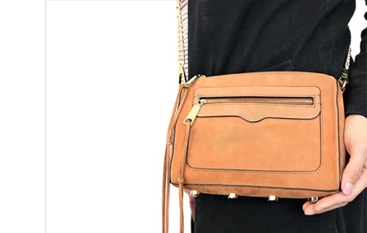 A photo of a small brown crossbody purse the purse is shown handing on someones shoulder with their hand holding the bottom of the bag