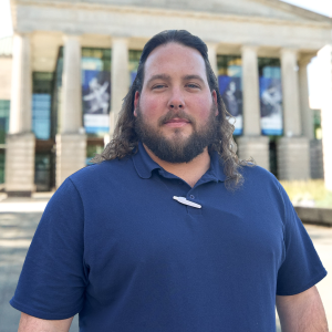 Headshot of Blade Perdue in front of the Martin Marietta Center for the Performing Arts wearing a blue button down.