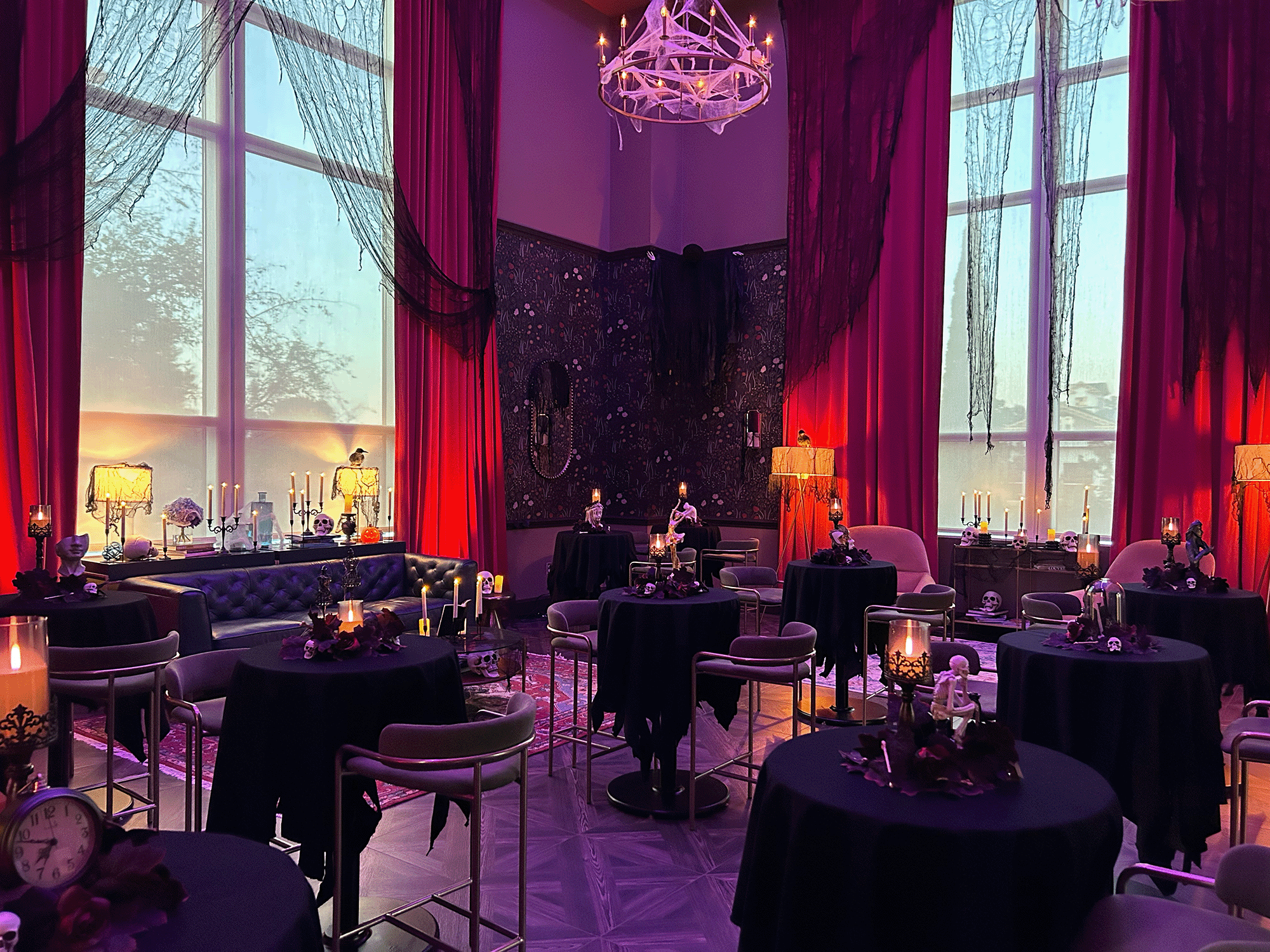 a photo of a dimly lit room there are cocktail tables and candles throughout the space there are two large windows on shown in the photo