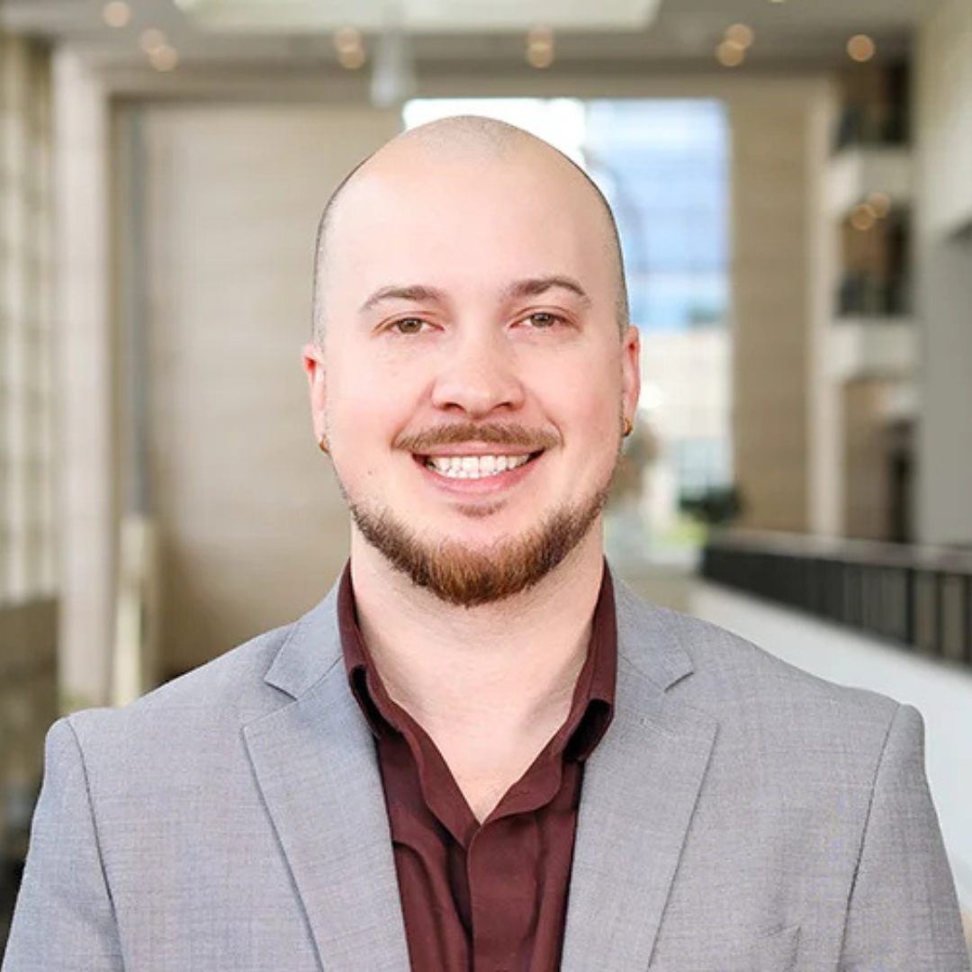 Headshot of Tristan Mulder in a grey suit with a red button down on.