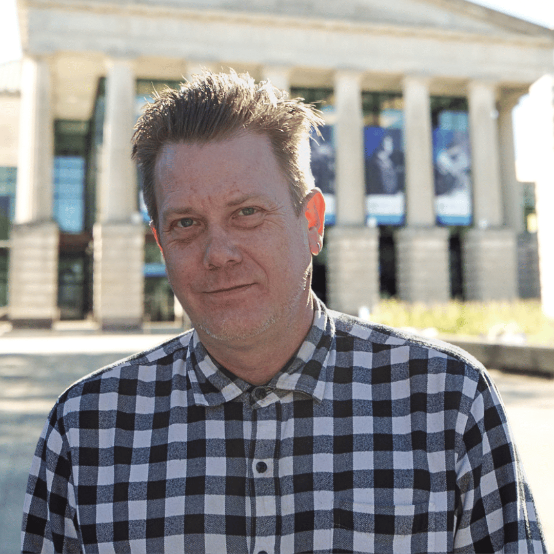 Headshot of Jason Morris in front of the Martin Marietta Center for the Performing Arts wearing a black and white checkered button down. 