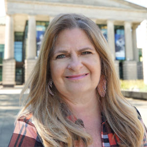 Headshot of Lisa Morgan in front of the Martin Marietta Center for the Performing Arts wearing a plaid shirt.