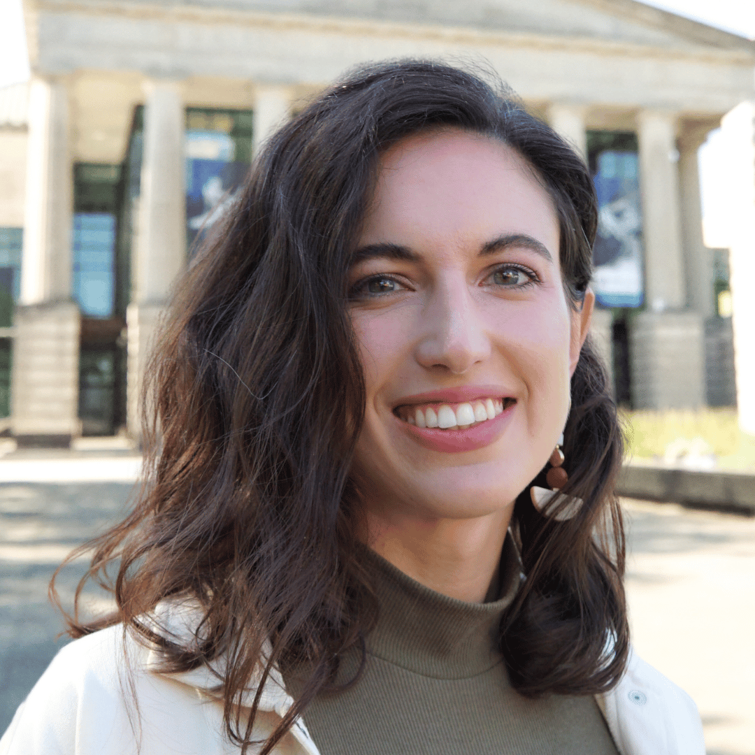 Headshot of Melanie Margarum in front of the Martin Marietta Center for the Performing Arts wearing a green shirt and white sweater. 