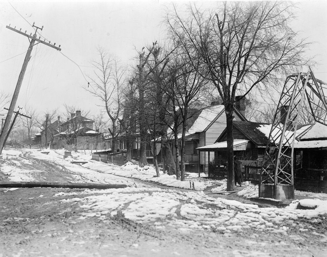 a black and white photo of a row of five homes is seen on the right side. there are power lines on the left side of the photo and snow is on the ground.