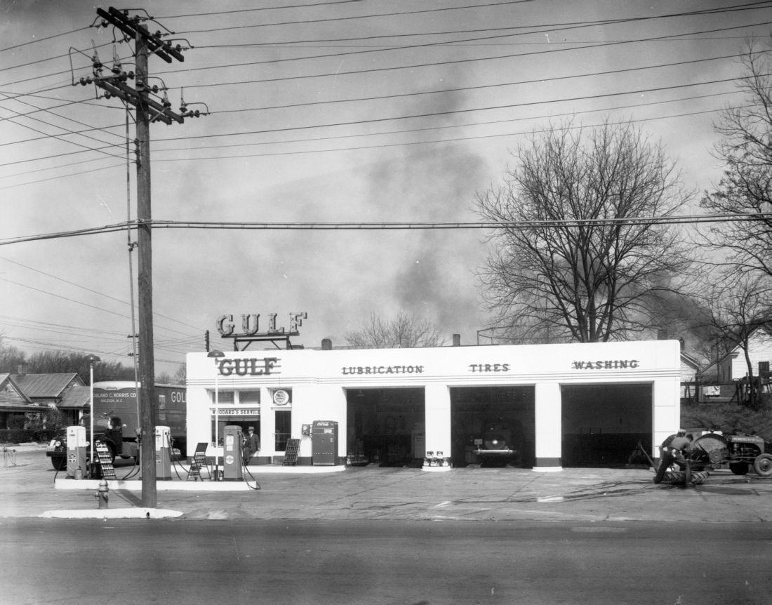 a black and white photo of a gulf fuel station there are three car bays shown there is a tree in the background and power lines and pole to the left of the image