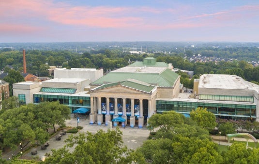 Aerial view of the Martin Marietta Center for the Performing Arts surrounded by trees under a pink and blue sky.