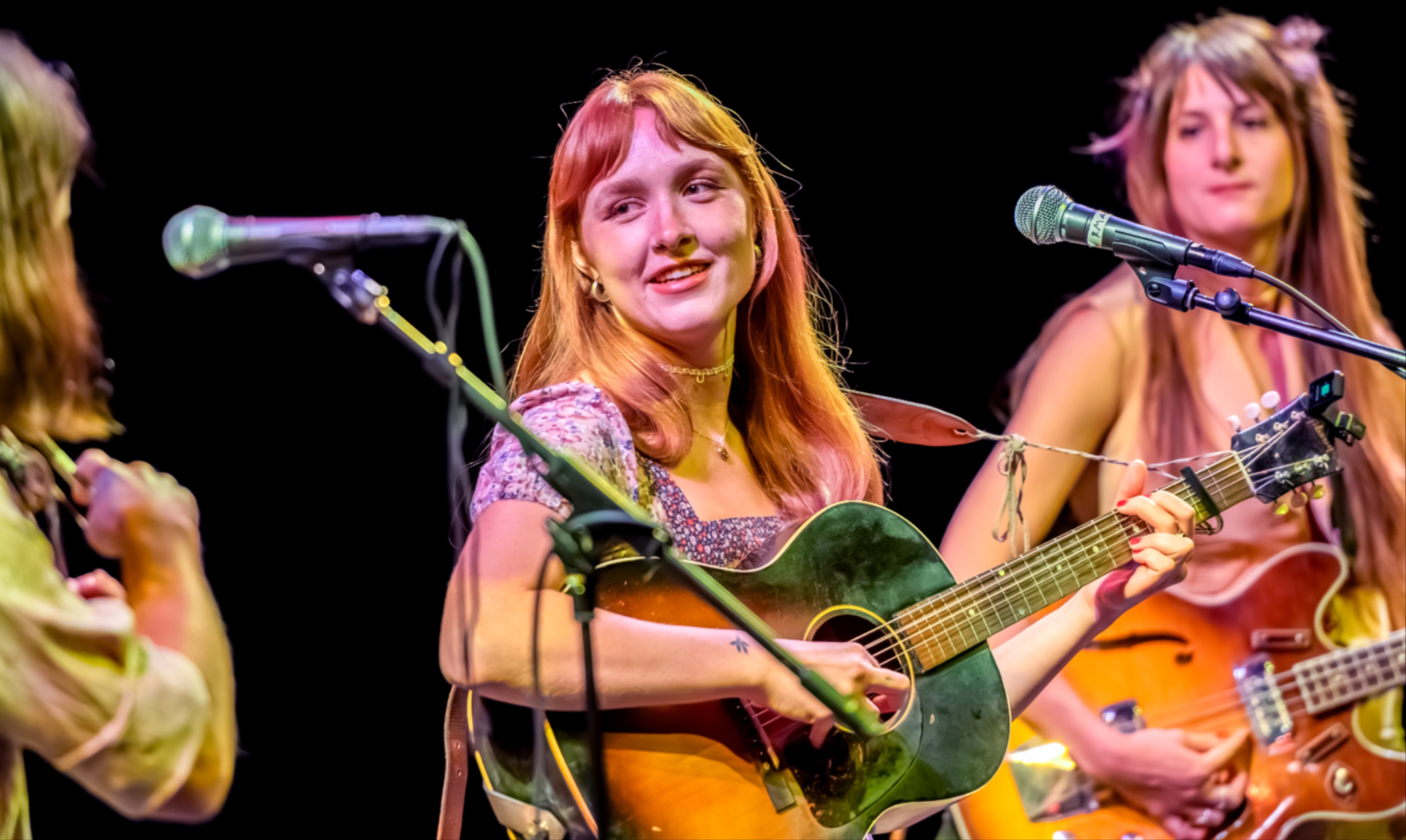 BellaWhite is shown playing a guitar she is looking slightly to her right and smiling