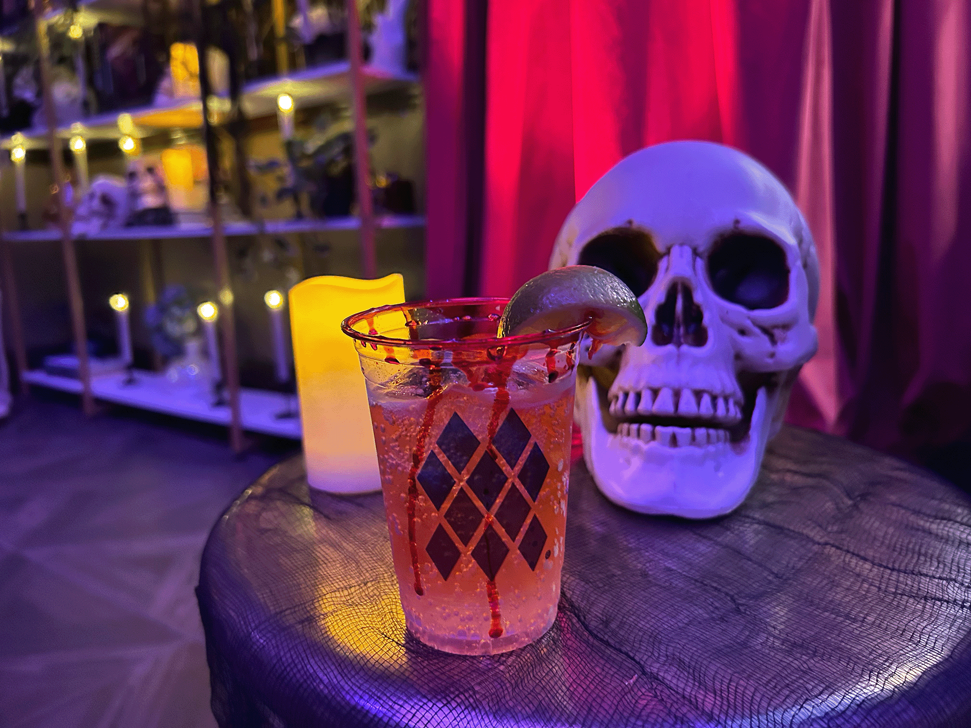 a photo of a cocktail on a table there is a skull and candle behind it