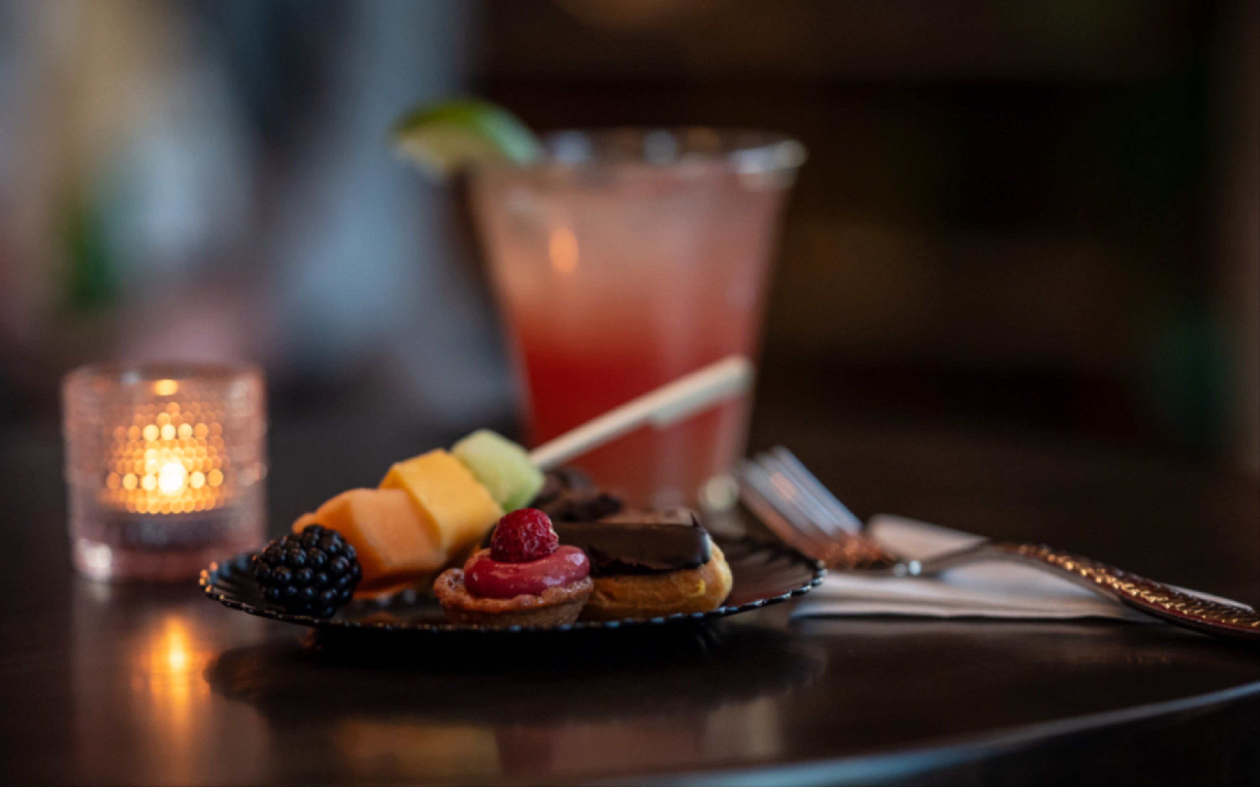 A photo of a drink and plate of food on a table, there is a small tea light candle shown in the background