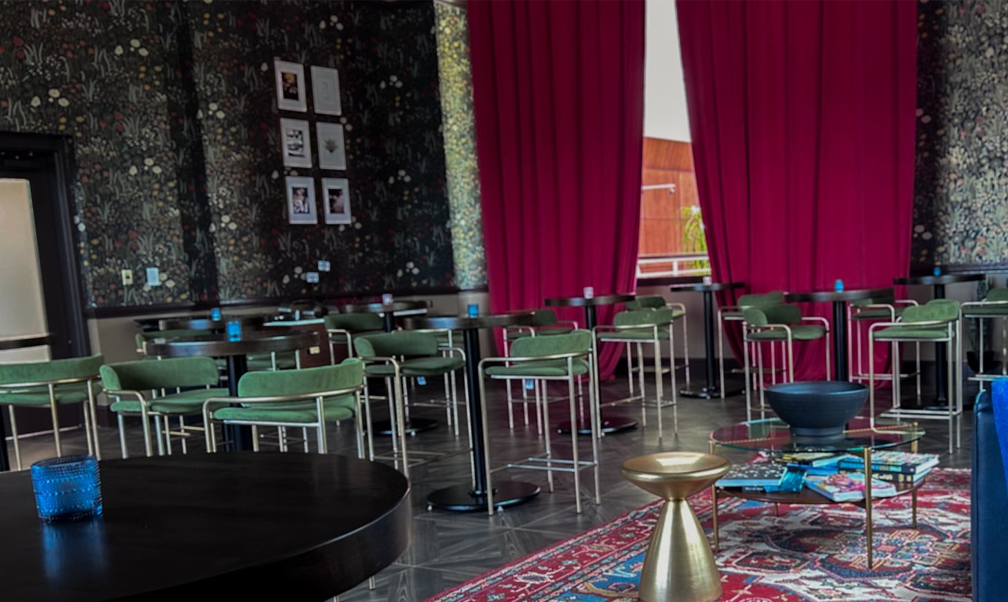 A photo of a lounge space there are red curtains hanging from the wall in the center and high top tables shown throughout the room
