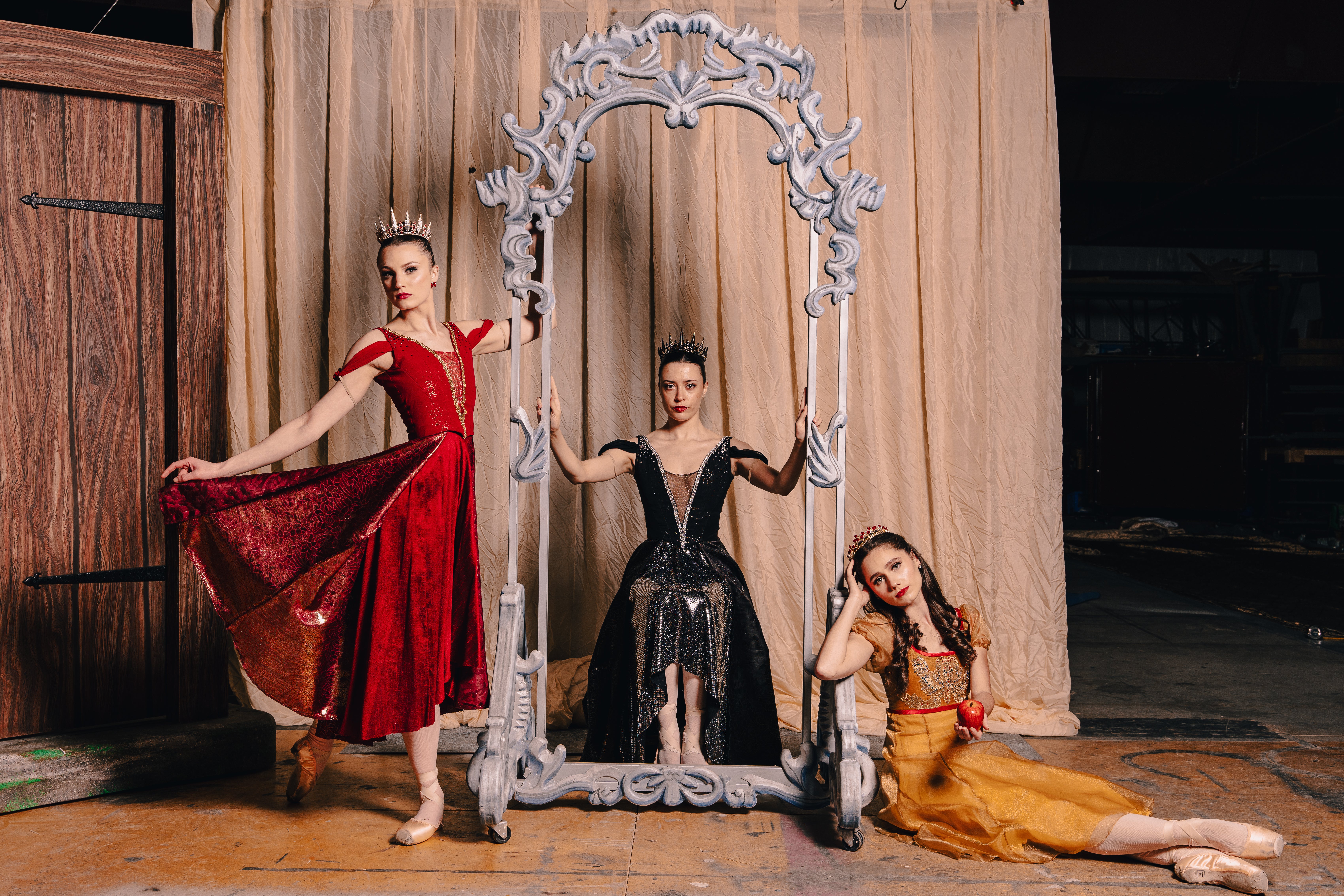 Three Carolina ballet performers are shown they are wearing formal dresses and crowns two are seated and one is standing