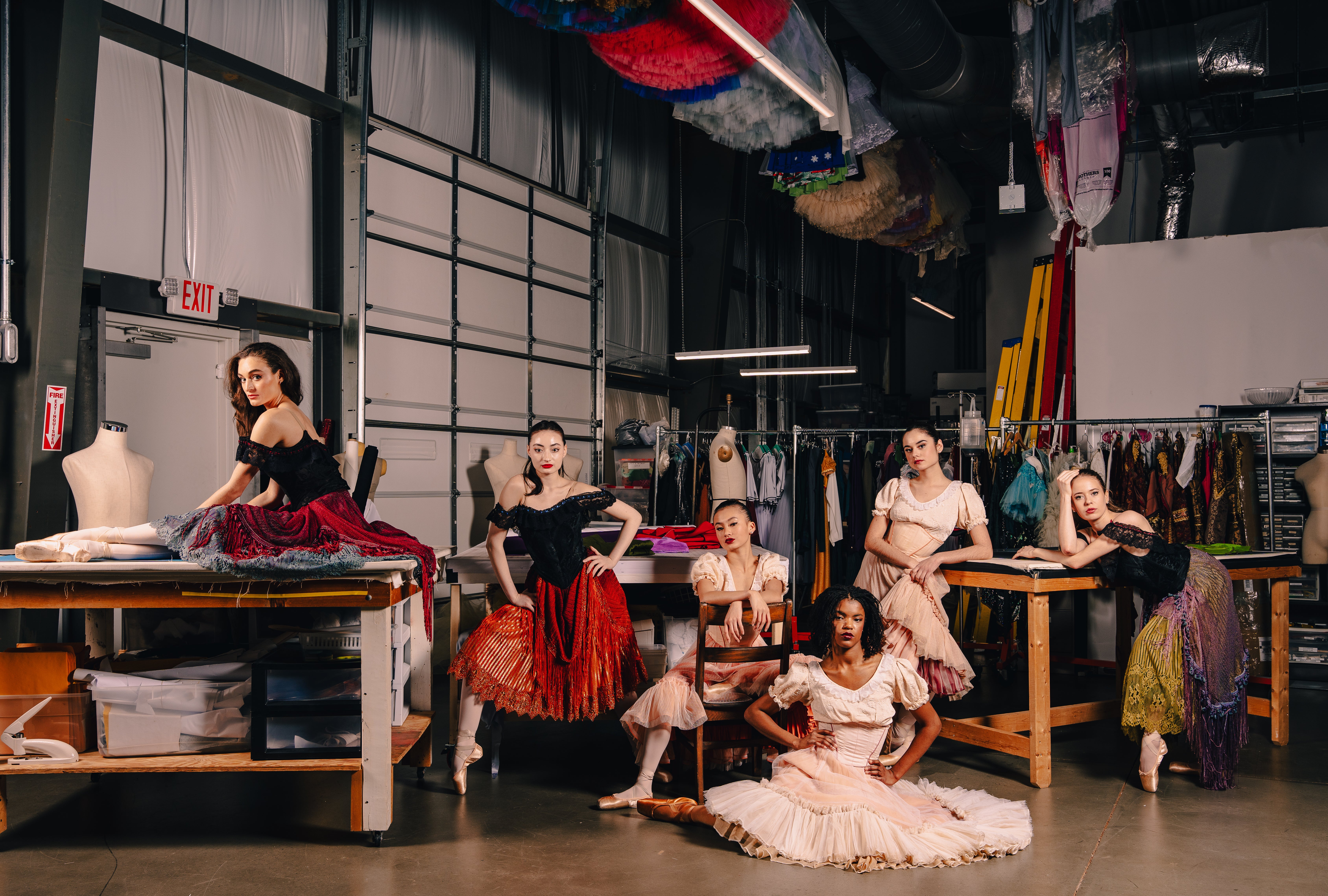A group of Carolina ballet performers sitting together amongst costumes in a warehouse