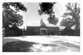 Black and white photo of the exterior of The Centenial school in Raleigh, NC in 1876 with trees and an open sky.