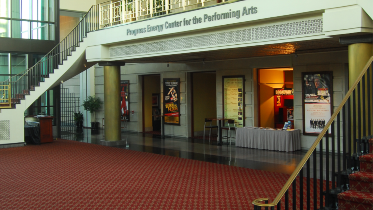 Interior lobby of Raleigh Memorial Auditorium photographed from 1990 with red carpet, a double staircase, and shows listed on marquees. 