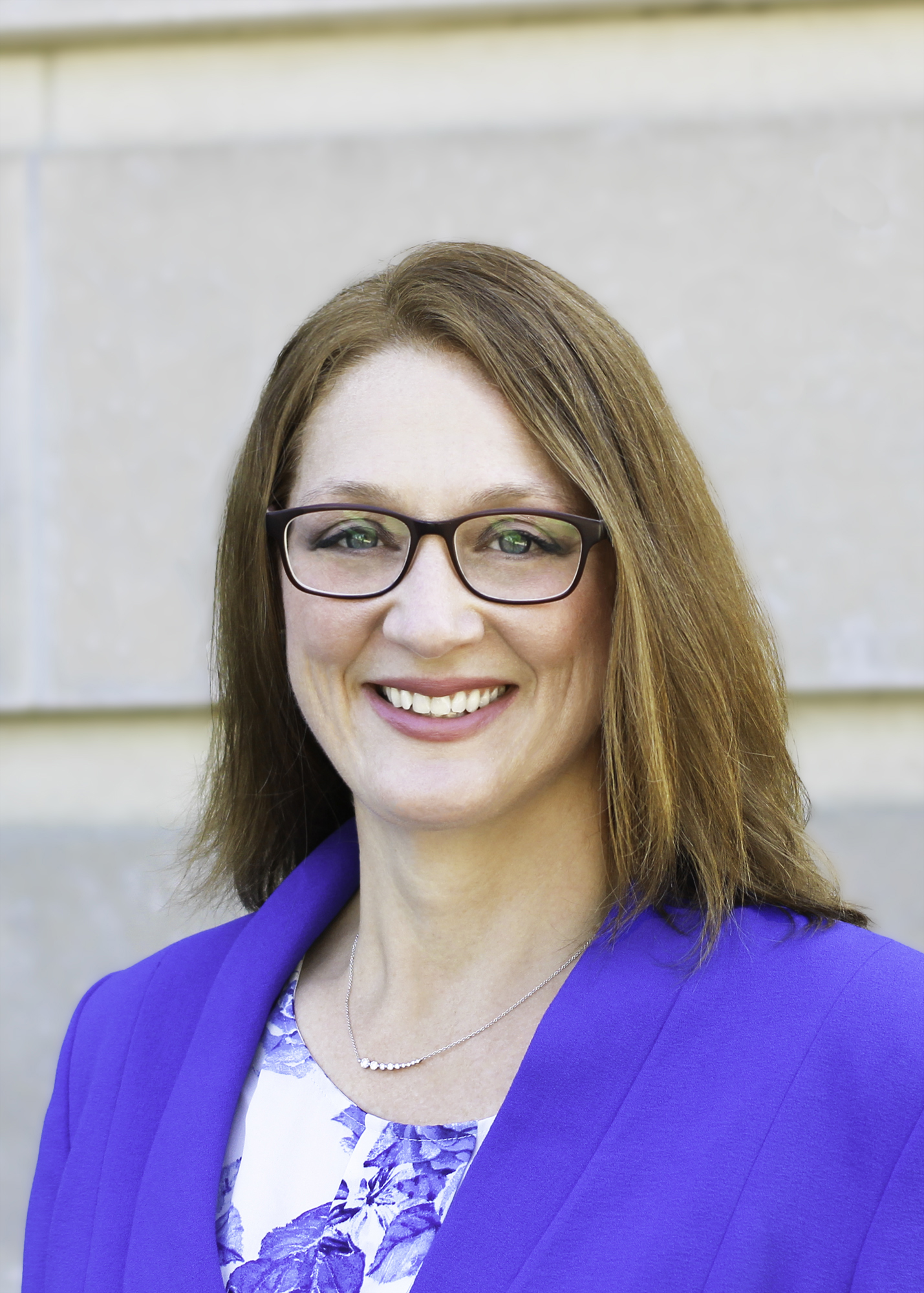 An image of Michelle Bradley in a bright blue sport coat. She is wearing glasses.