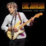 an image of guitarist Eric Johnson. He is standing against a black background and holding a yellow electric guitar, standing in front of a microphone looking slightly to his right. The words Eric Johnson Treasure Tour 2022 are in the upper right corner in yellow