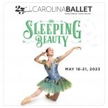 Ballerina kneeling on one knee with the other leg stretched and arms in the air, wearing in a blue and green dress.