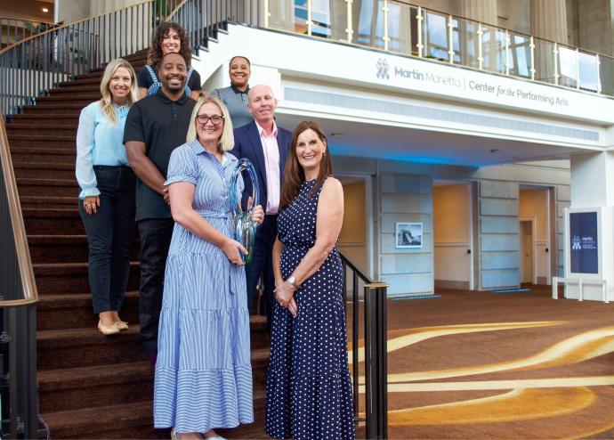A photo of venue staff standing on a staircase, Michelle Bradley is shown in the front holding a large glass award