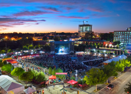 A photo of Red Hat Amphitheater with the sunsetting in the background and lights on the stage