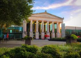 Outside photo of the front of Raleigh Memorial Auditorium, there is a tree in the left frame of the photo and a garden directly infront of the building