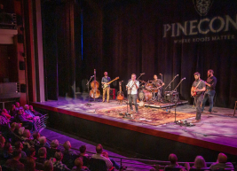 A photo of the A.J. Fletcher Opera Theater stage. There are multiple performers shown playing instruments in front of an audience