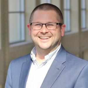 A photo of Brian Clark he is wearing glasses and a grey blazer
