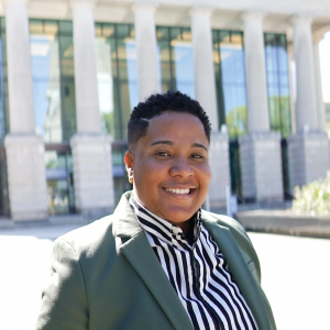 a photo of BRITTANY WASHINGTON she has short brown hair and is wearing a striped shirt and dark green sport coat