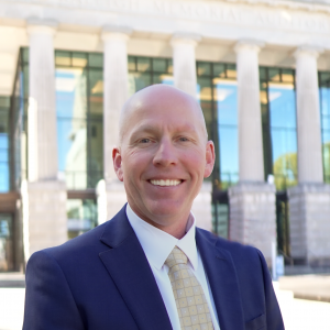 a photo of Chris Bullock he is a wearing a white shirts, yellow tie and navy sport coat