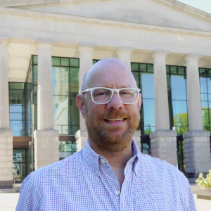 a photo of Dave McManu he is wearing glasses and has on a striped button down shirt