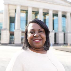 a photo of Keisha peacock she has brown shoulder length hair and is wearing a white blouse