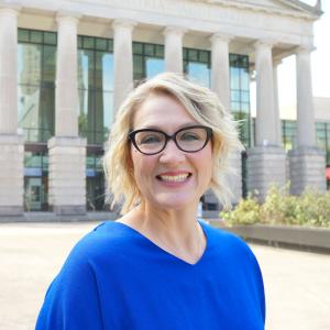 a photo of Michelle Bradley she has short blonde hair and glasses and is wearing a bright blue blouse
