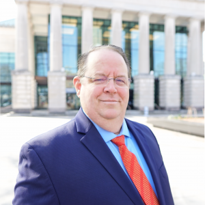 a photo of Robert Leavell he is wearing glasses and a light blue button down, red tie and navy sport coat