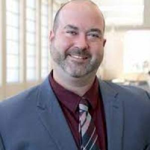a photo of Brad Clinton he is wearing a maroon button down with a plaid tie and a grey sport coat