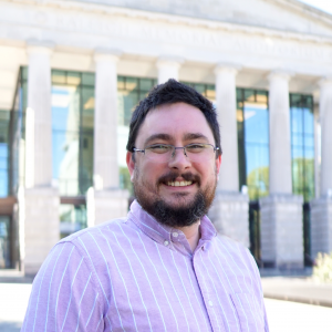 A photo of Lucas Johnson he has brown hair and glasses and is wearing a pink button down shirt