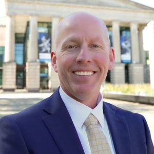 a photo of Chris Bullock he is a wearing a white shirts, yellow tie and navy sport coat